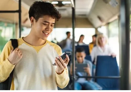 A male student smiling at his phone while riding his school bus